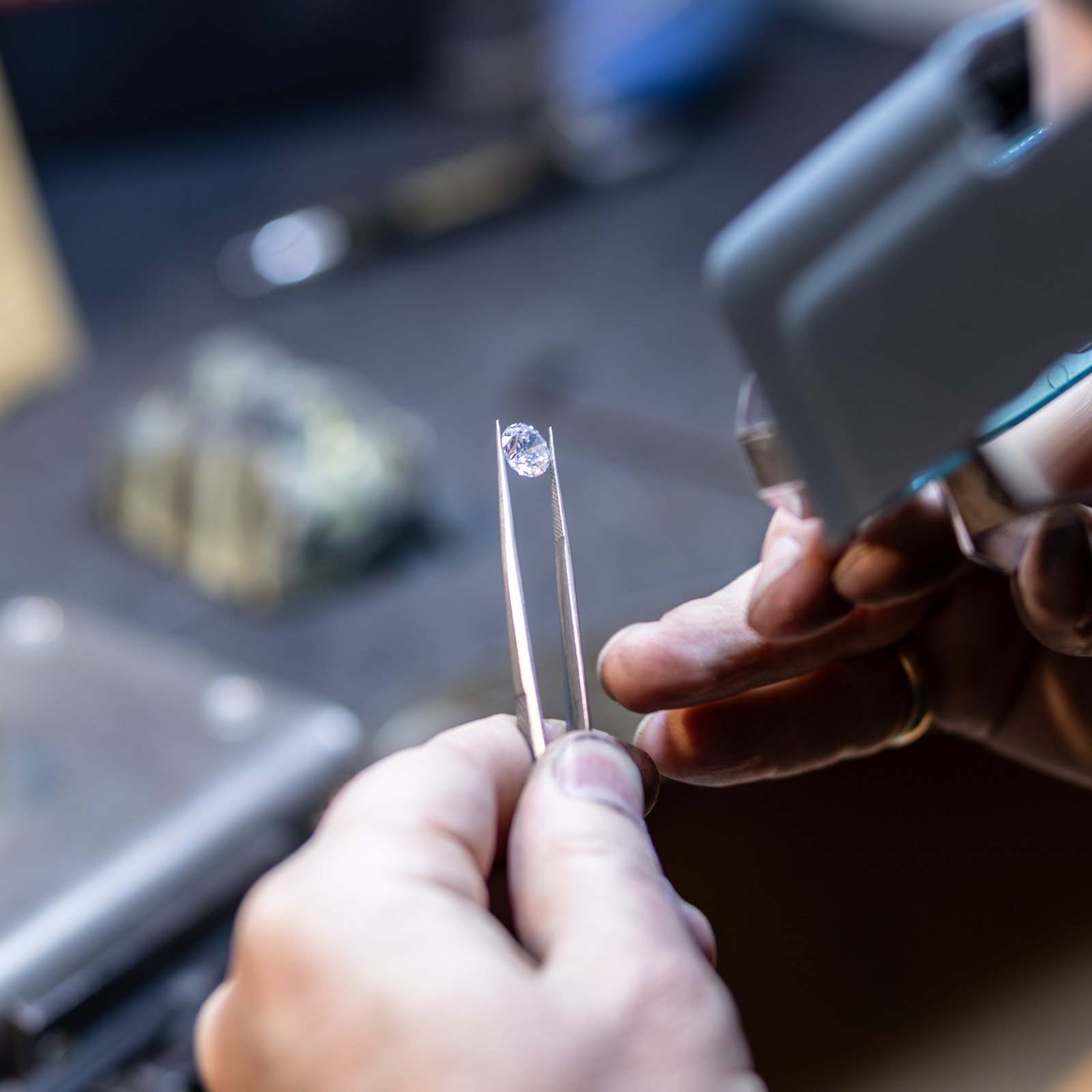 A loose diamond held in tweezers and examined through a loupe at the bench